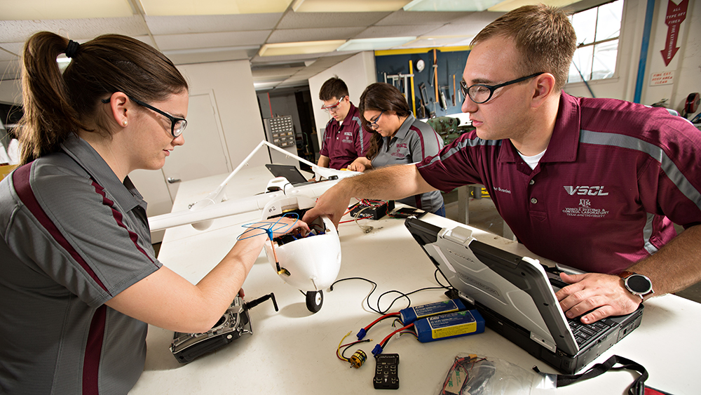 Students assemble a small aircraft in an engineering lab using electronic components, testing equipment and a laptop