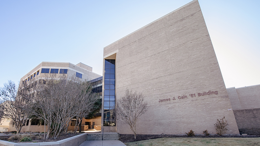 two buildings connected by an elevated glass walkway, where the closer building (on right) features the words James J. Cain '51 Building