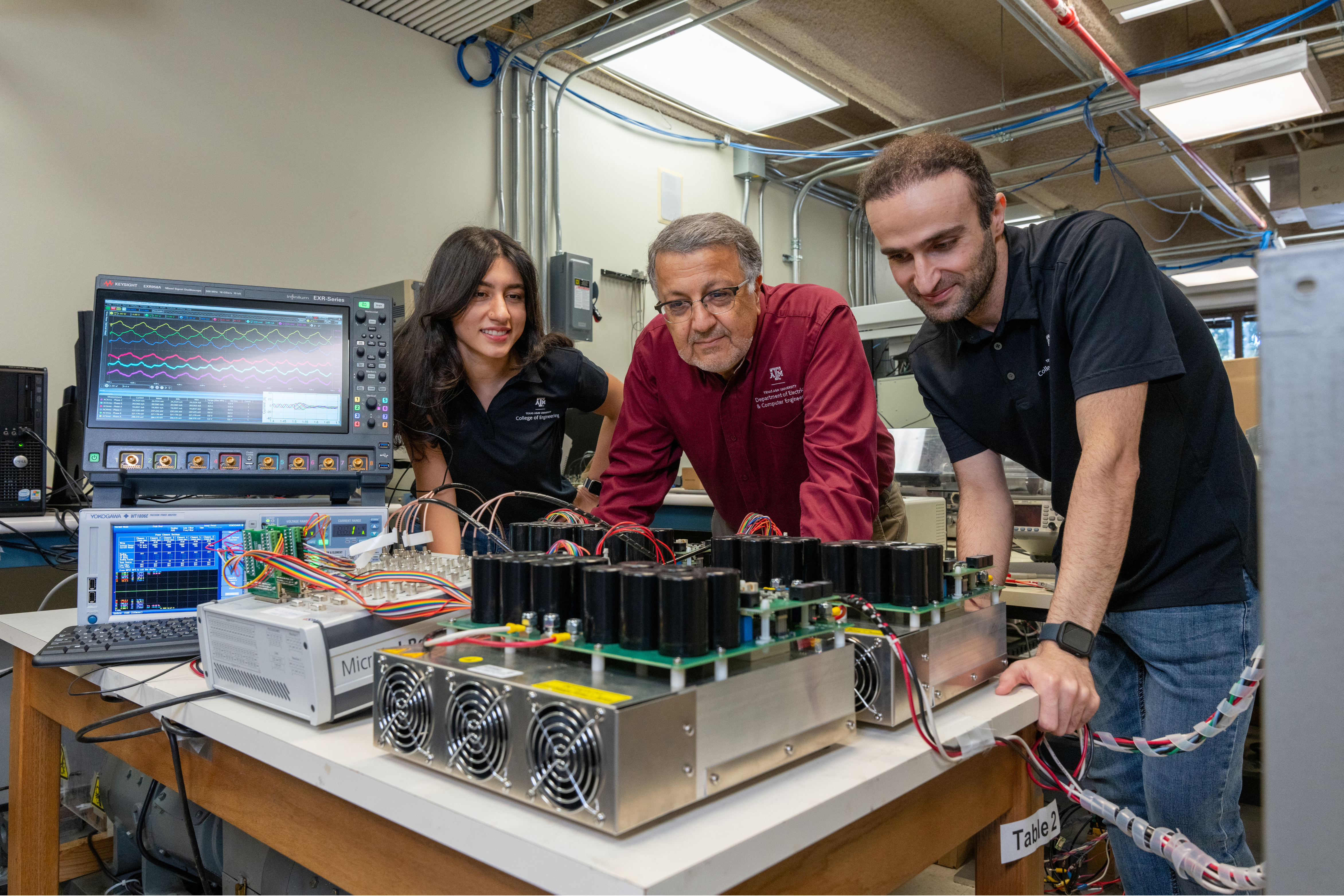 Three people standing over electrical components.