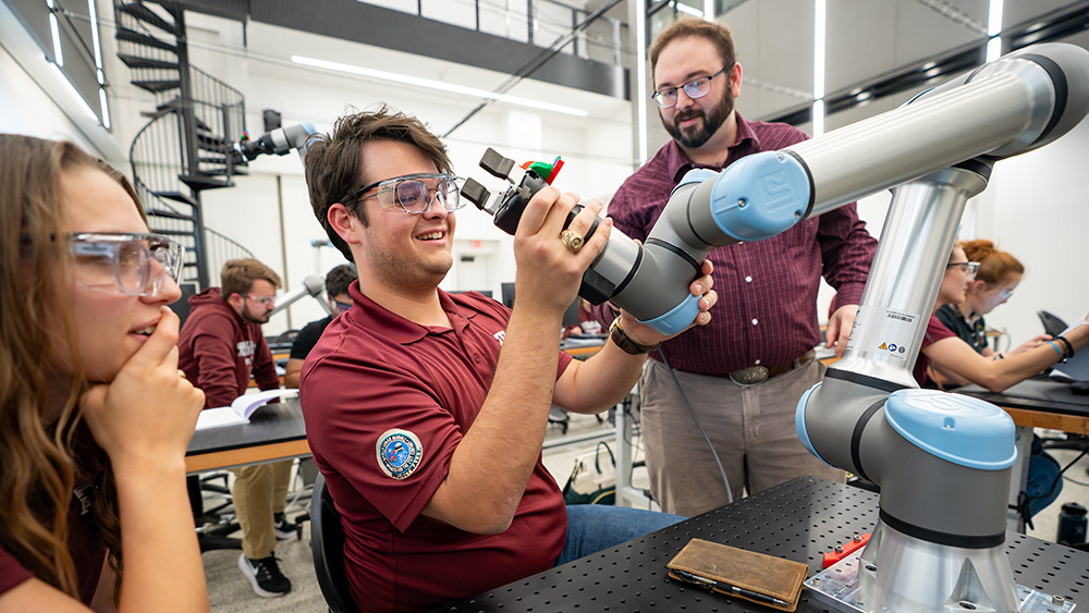 A student working with a robot arm while a professor and another student look on.