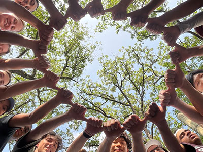 twenty students stand in a circle, make the Aggie thumbs up sign sideways, then touch their thumbs to the next person's fist to form an Aggie thumbs up ring