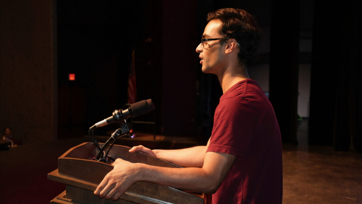 A male student stands at a podium on a stage.