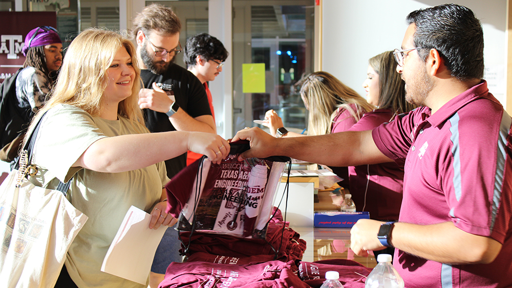 Female student reaches across the table to collect her new student packet from an Engineering Academy staff member. 