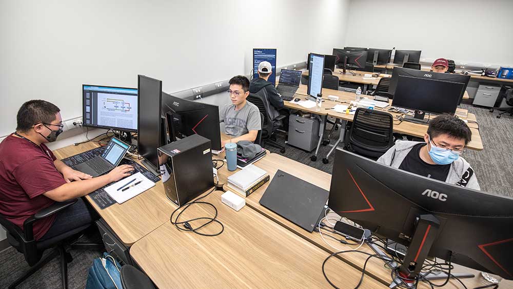 five male students using individual workstations within a large computer lab.