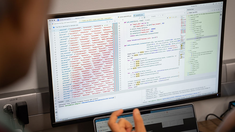 A human hand gestures in front of a computer screen filled with cybersecurity coding text
