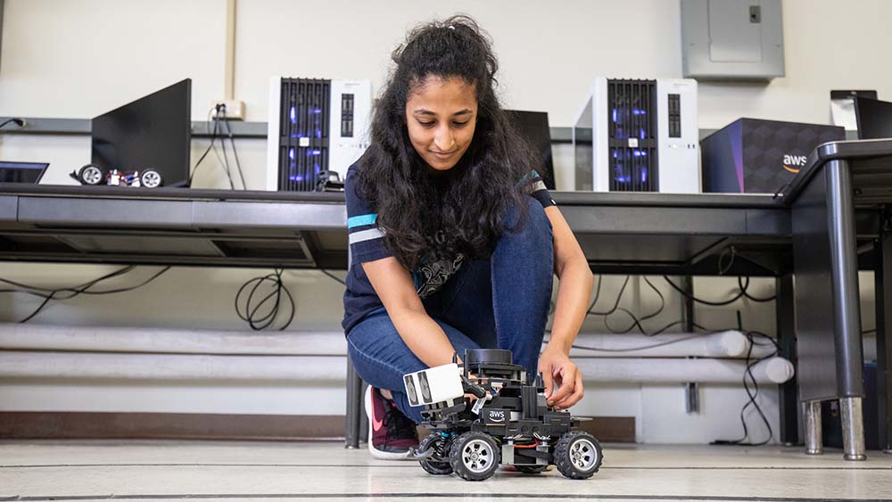 A woman kneels over and works on a small vehicle in a lab.