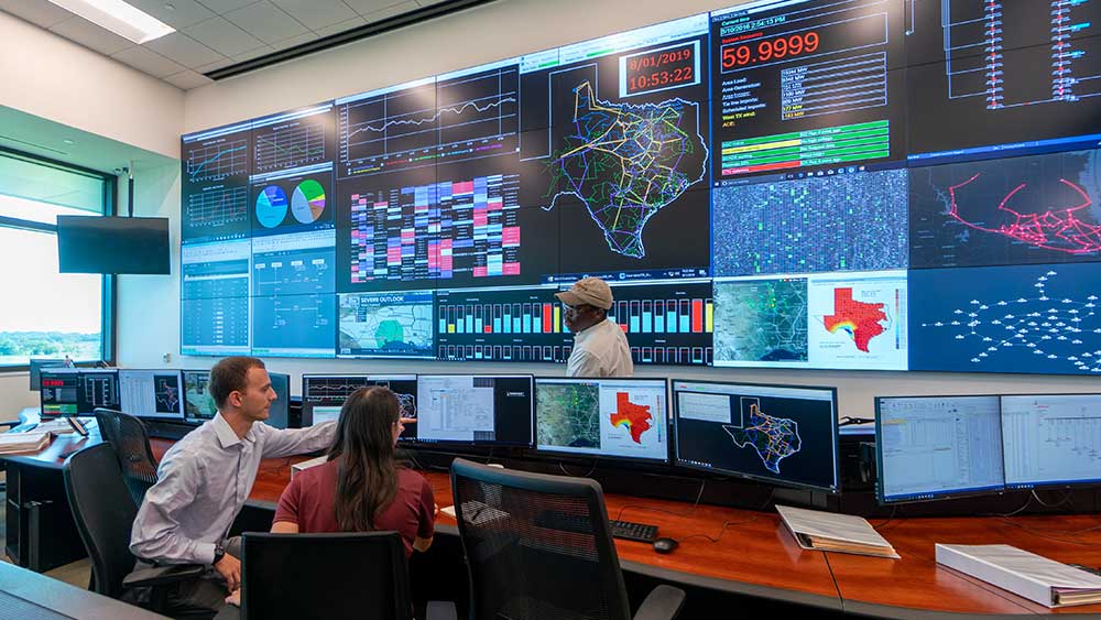 roomful of monitors and wall screens showing data for Texas with a man and woman seated at computer and another man looking at them.