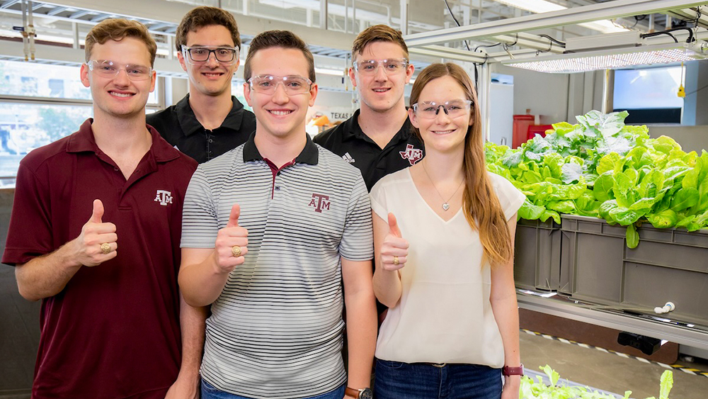Five students smiling in a lab, wearing protective eye gear.