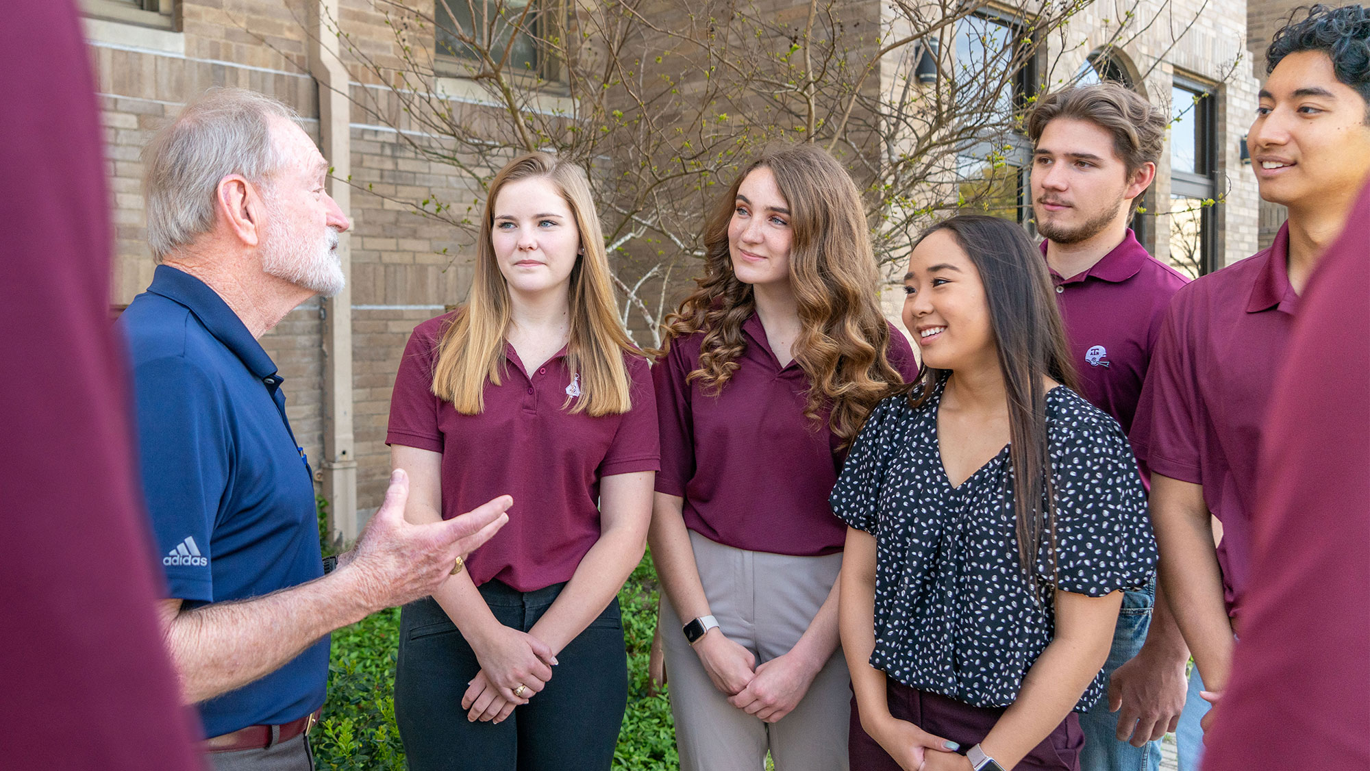 A group of students standing outside listening to a professor speak