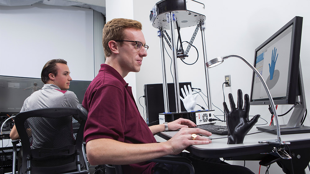 Two male students looking at a computer screen and a model of a hand