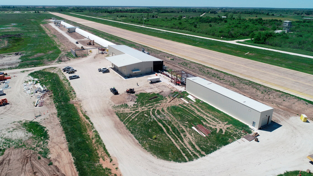 An aerial view of four metal buildings in a row. Three are connected by two long, semi-round tunnels, and one is a long, narrow rectangle. 