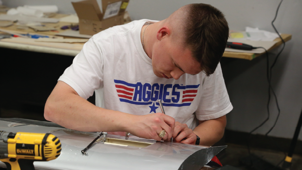 student working on a wing wearing a shirt that says aggies