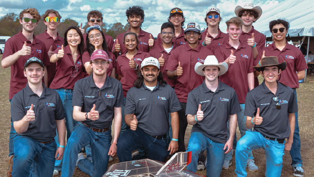 Team of aerospace engineering students holding their thumbs up and facing the camera wearing maroon polos