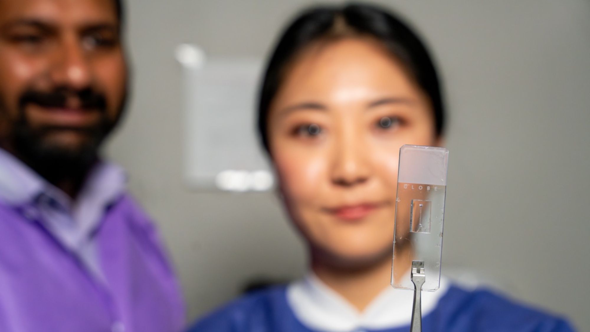 Two researchers looking at a transparent chip held in tweezers.