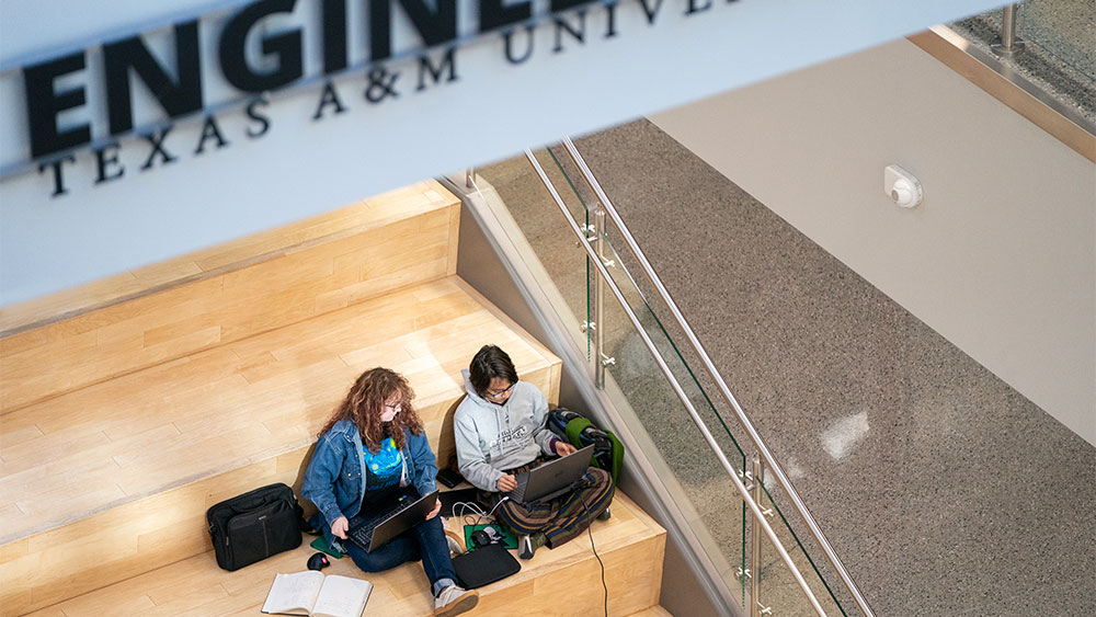 Two students sitting on a staircase and looking at their laptops. 