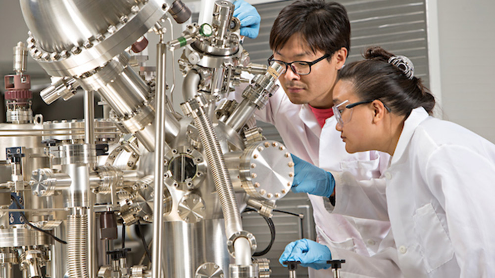 A male and a female standing looking through a giant silver telescope