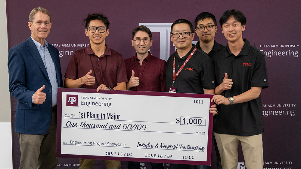 Six people standing and smiling, holding up a check for $1000.