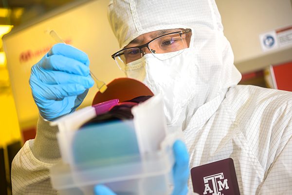person in protective lab wear studying a thin circular disc