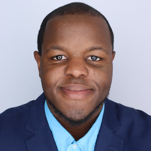 A headshot of Dr. Joshua Peeples, wearing a navy blue blazer against a light gray background. 