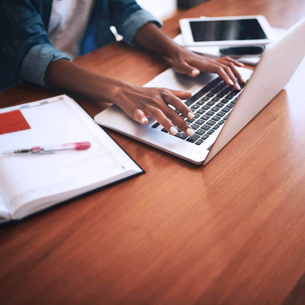 Woman using her laptop (with a notebook at her side) to get her engineering master's degree online.