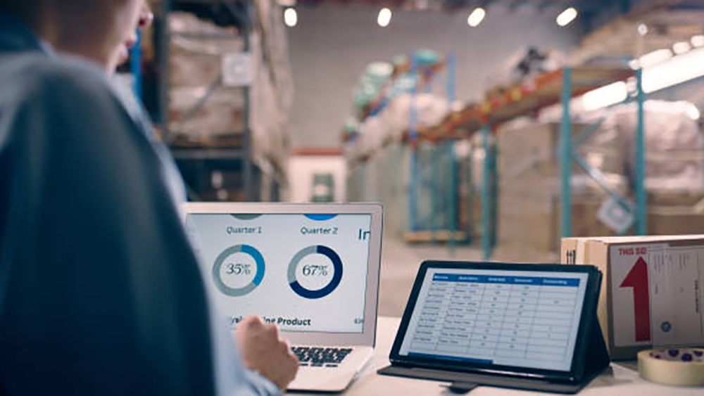 A person looks at two computer screens in a warehouse setting.