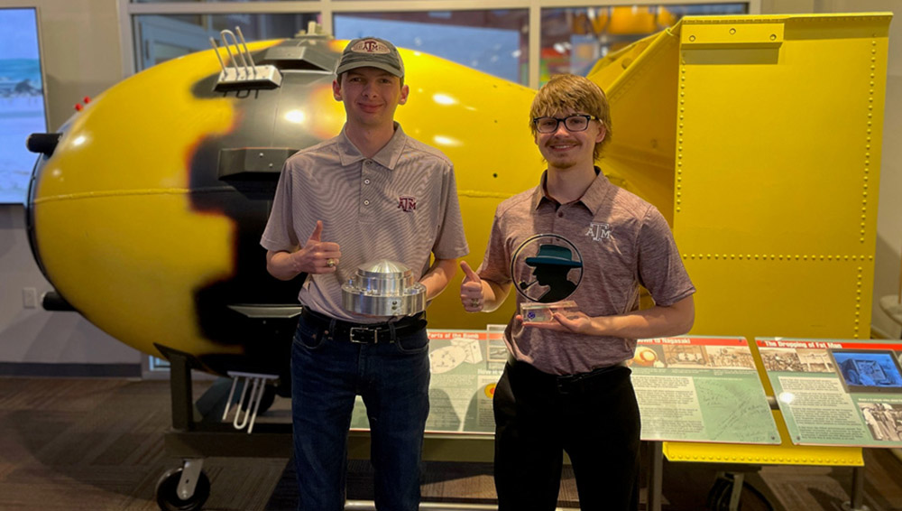 Two students give a thumbs up while holding trophies.