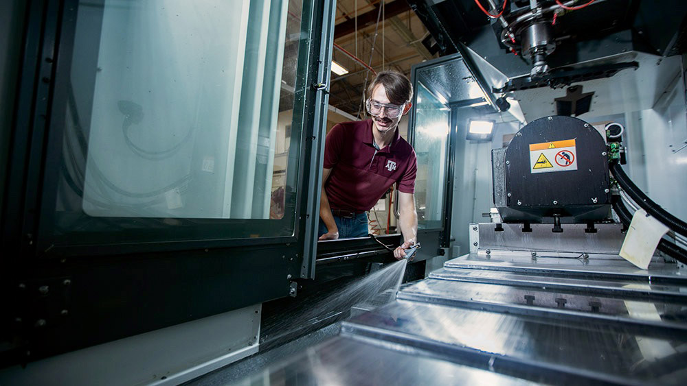 A student wearing safety glasses sprays water inside a machine.