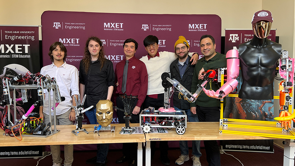 A group of five individuals in a lab with a variety of robots.