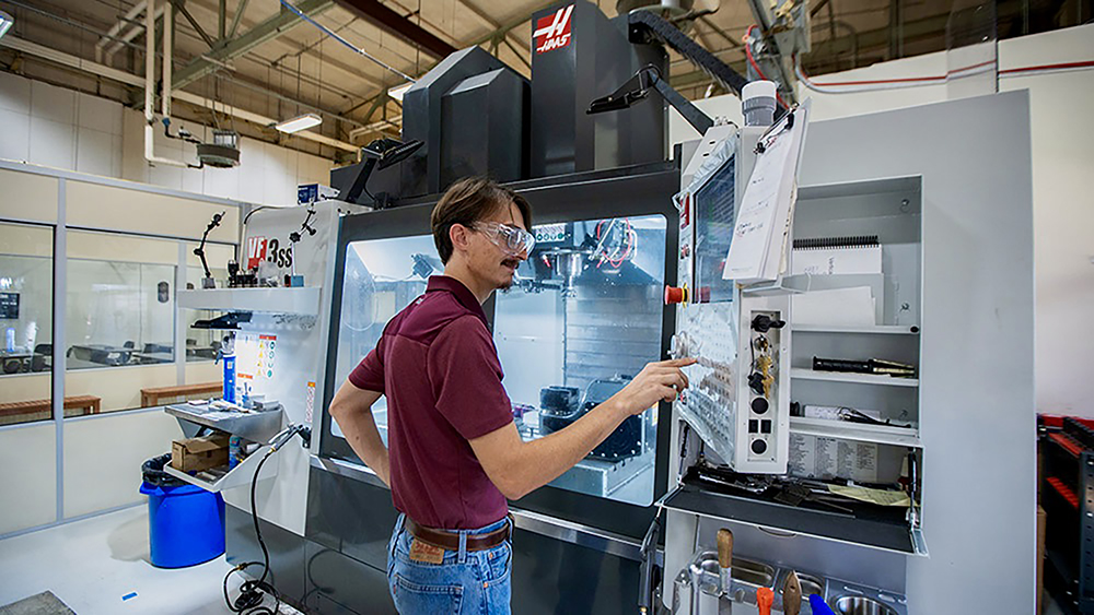 A student wearing safety glasses presses buttons on a large machine in a laboratory.