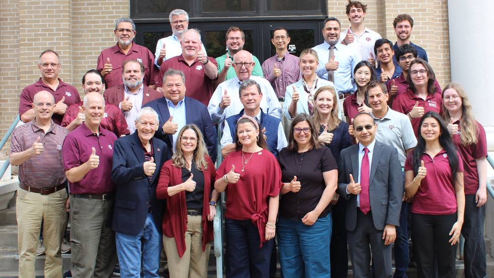 A large group of individuals who are smiling and giving thumbs up pose in rows on a staircase.