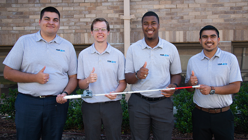 Four individuals in matching blue polos smile while giving thumbs up and holding a white and red pole.