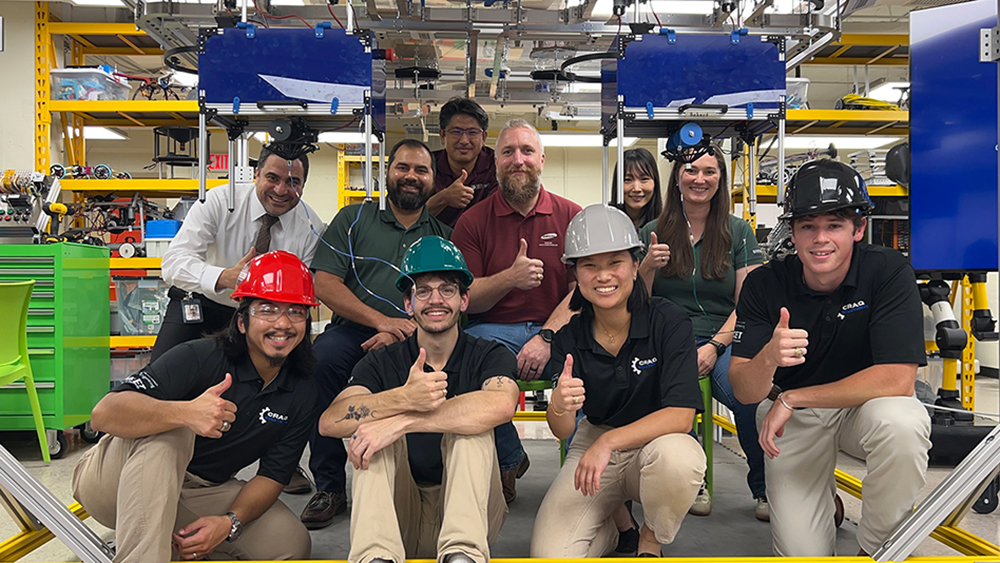 A group of ten individuals, some wearing hard hats, pose in a laboratory setting.
