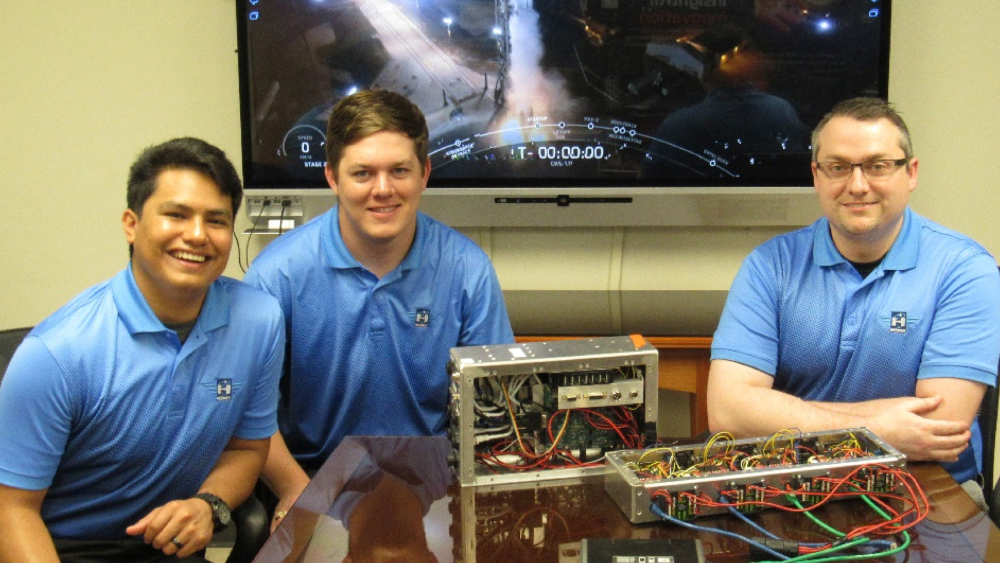 Three individuals in matching blue polos pose with electronic equipment.