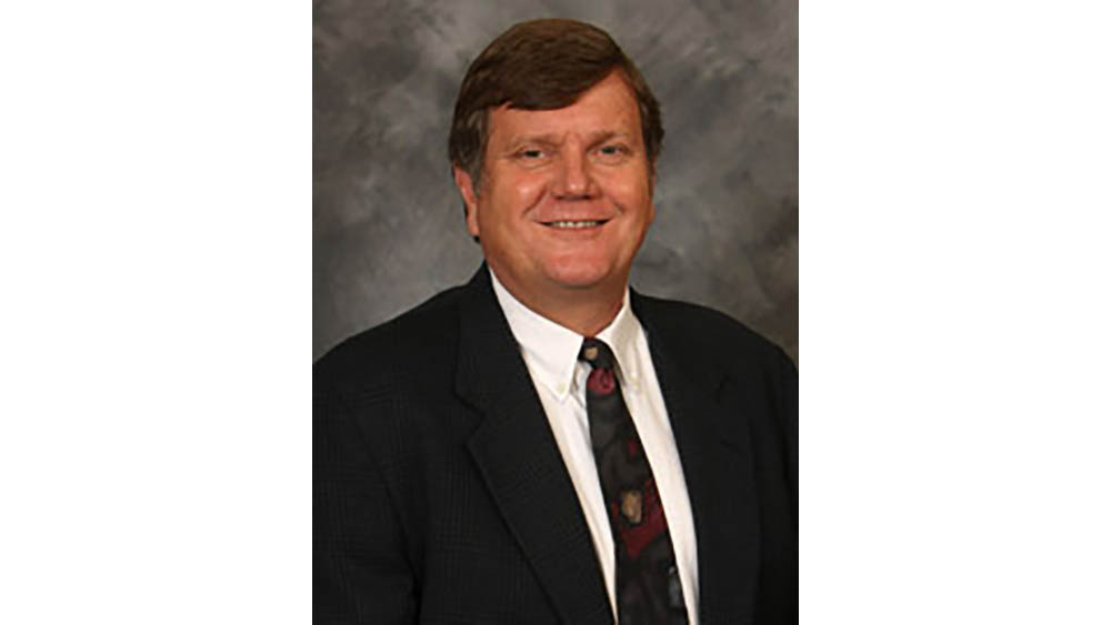 A smiling man wearing a dark suit and tie with a white shirt