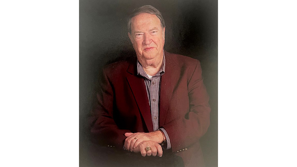 An individual in a maroon jacket and checked shirt poses for the camera.
