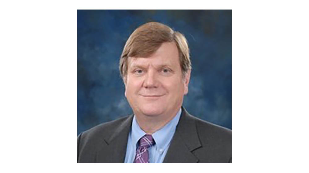 A man wearing a dark suit, blue shirt and tie