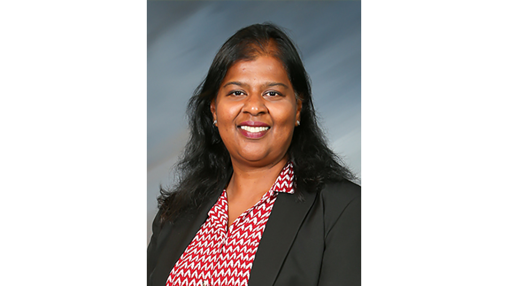 A smiling woman wearing a black jacket and red patterned blouse