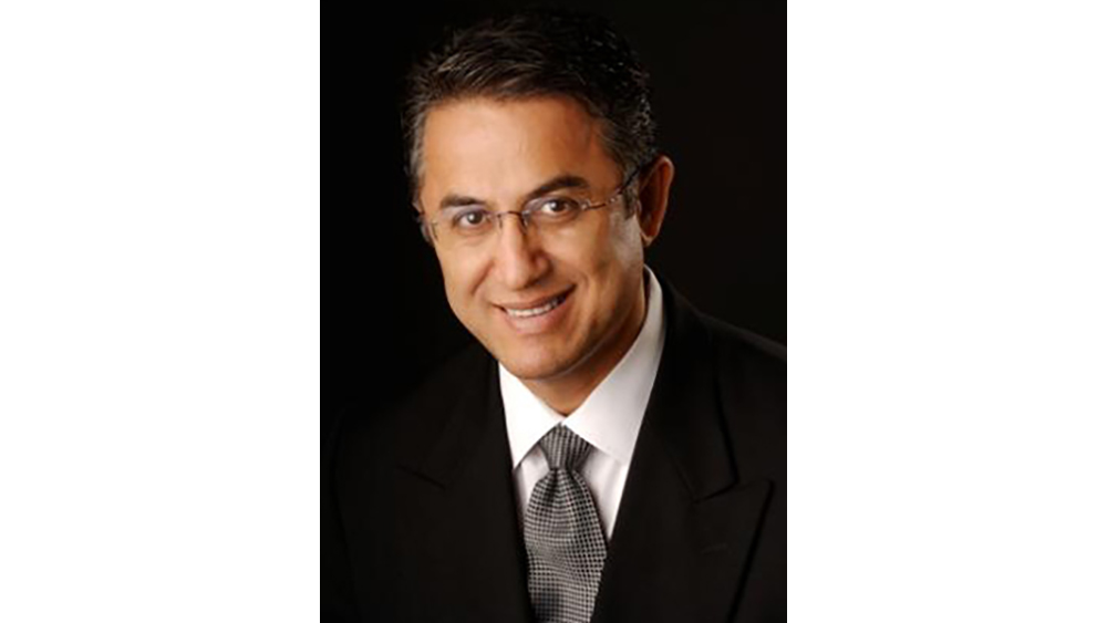 A smiling man wearing glasses and a dark suit