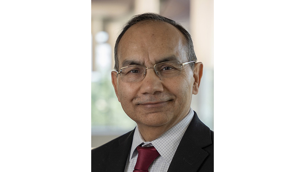 A smiling man wearing glasses, a dark suit and maroon tie