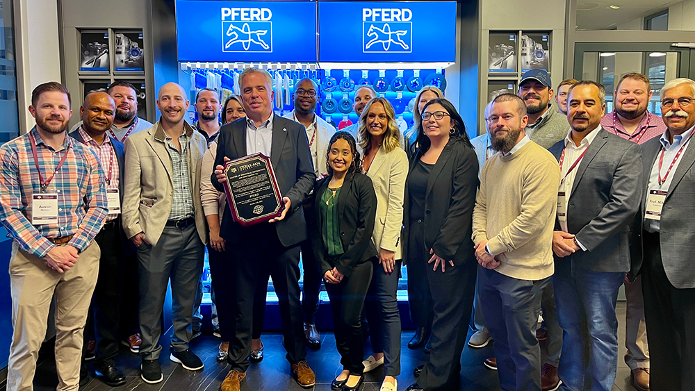 Large group of smiling people standing in front of a large display cabinet showing the logo of the PFERD company.