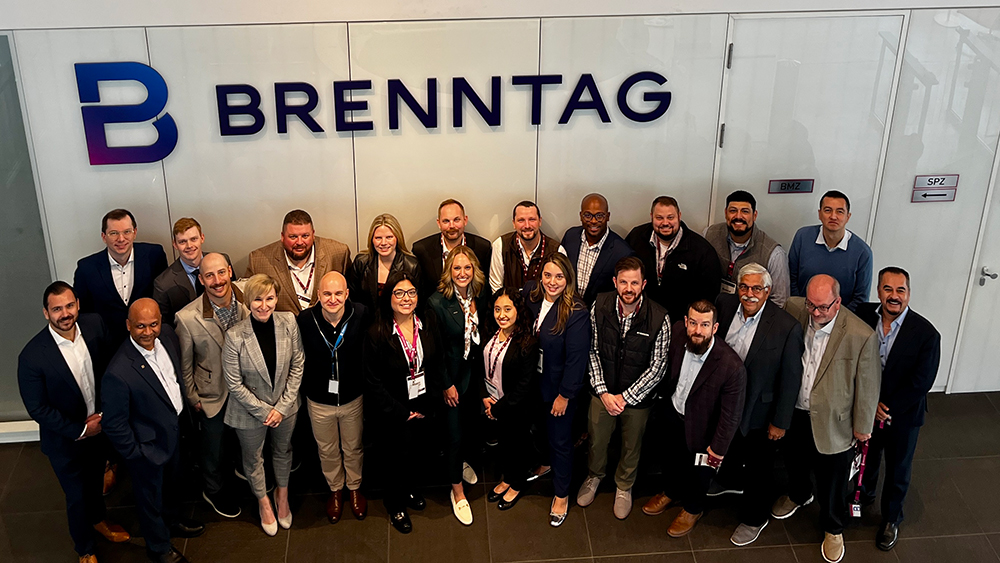 A large group of people smiling and standing in front of a wall featuring the Brenntag company logo.