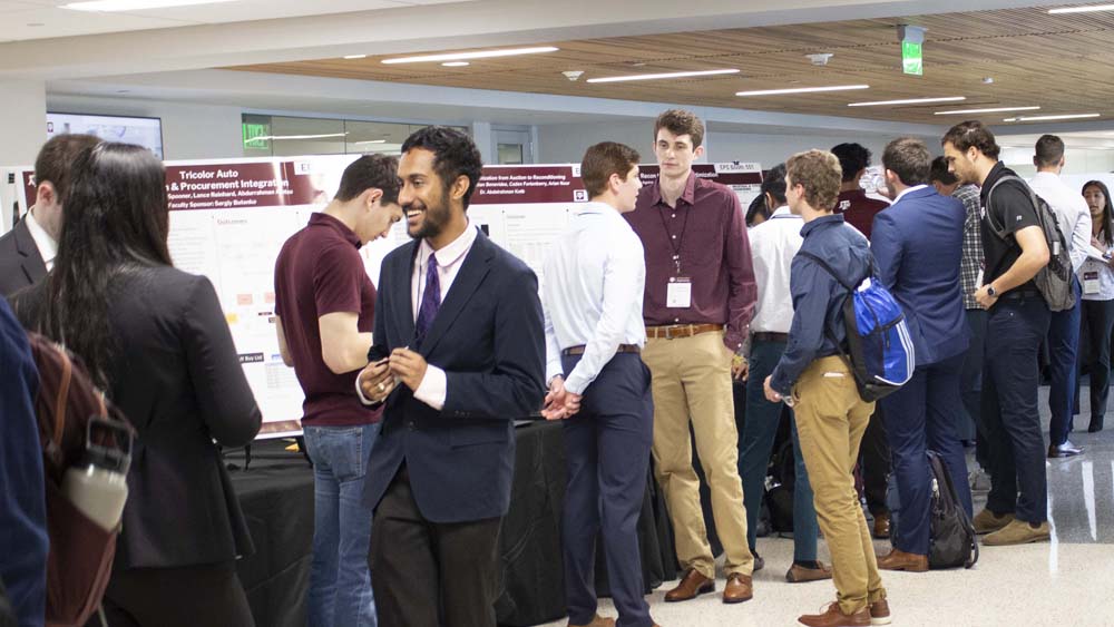 Students present their capstone posters in a large hallway.