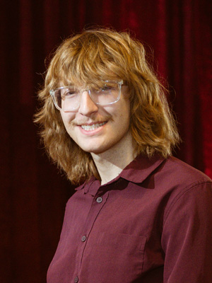 A man with glasses in a button up shirt in front of a background. 
