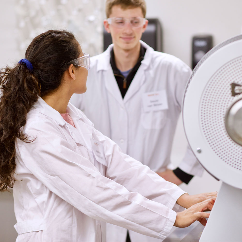 student researchers with safety glasses on looking at each other while working in a materials research lab