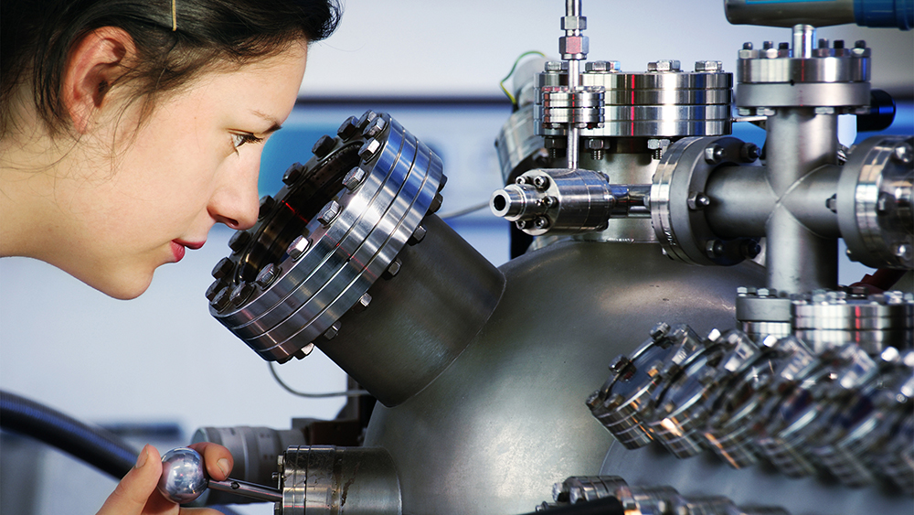 student peers into a small port on a metal tank