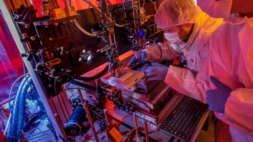 Man in white lab coat looking at microscope in lab