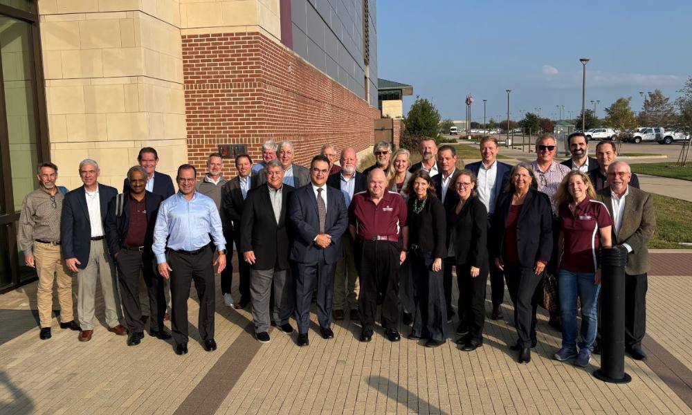 A group of people pose in direct sunlight outside a building. 