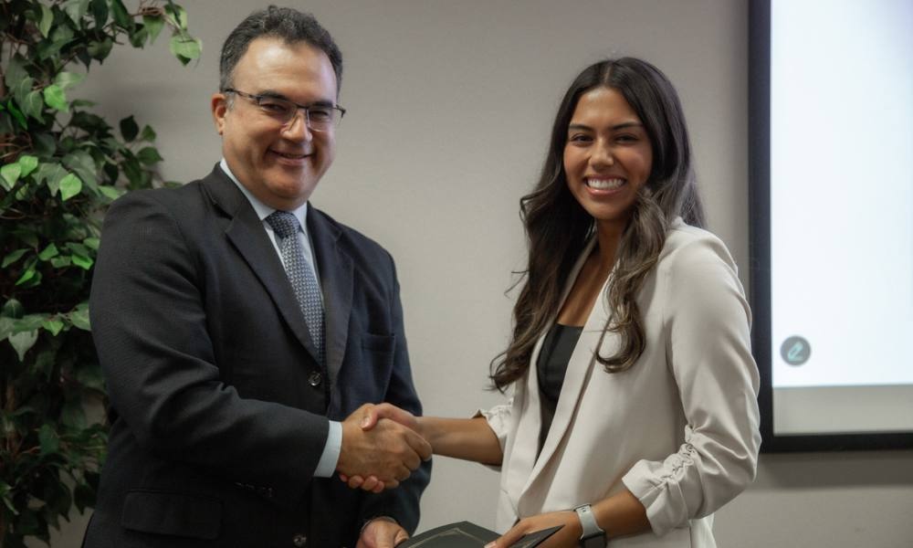Two people stand in a conference room and pose mid-handshake. 