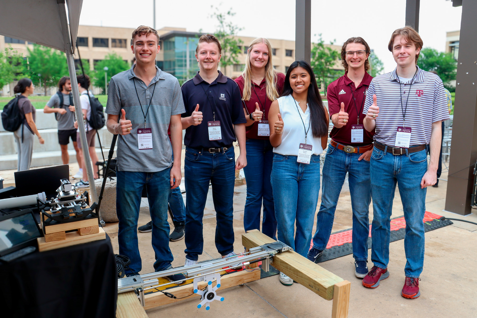Six students pose with thumbs up behind their engineering project.