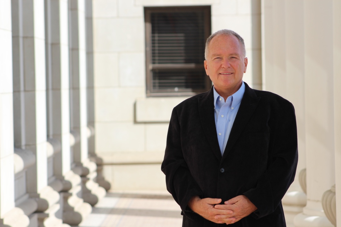 Dr. Laszlo Kish stands outside of building in black suit.